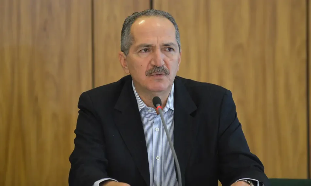 A foto mostra o ex-ministro da Defesa, Aldo Rebelo, em entrevista. Ele é um homem branco com cabelos grisalhos e bigode.