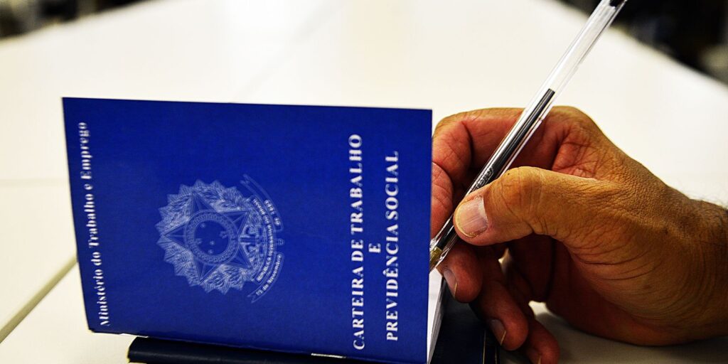 Mão assinando a Carteira de Trabalho