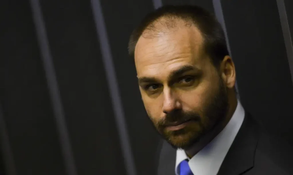 A foto mostra o deputado licenciado Eduardo Bolsonaro. Ele é um homem branco, calvo com olhos claros.