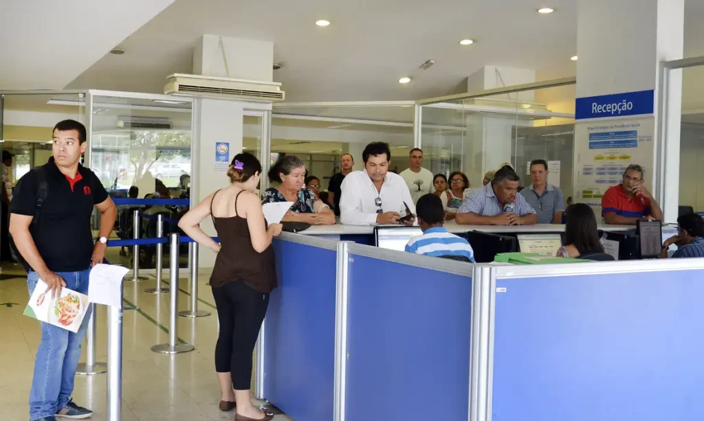 A foto mostra pessoas aguardando atendimento em agência do INSS.