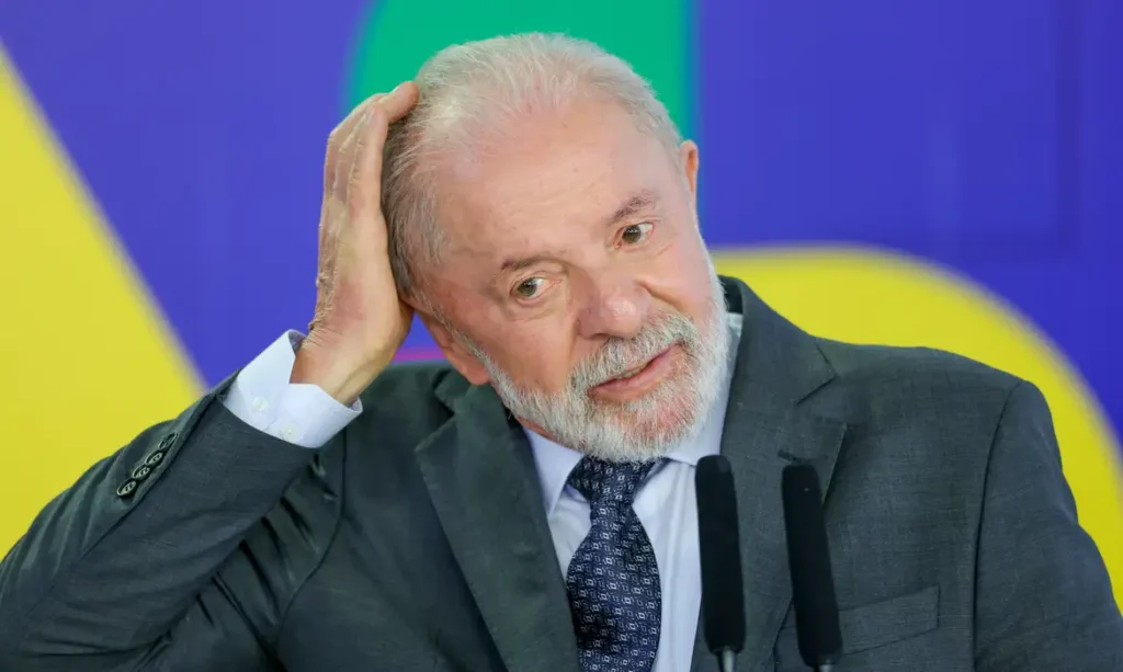 A foto mostra o presidente Lula durante entrevista coletiva no Palácio do Planalto. Ele é um homem branco, calvo e usa terno cinza escuro.