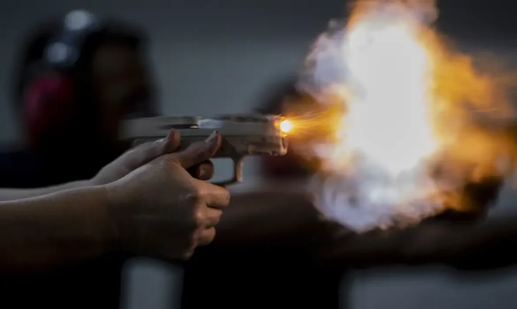 A foto mostra uma pessoa com uma arma nas mãos, fumaça e pólvora.