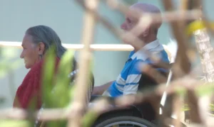 A foto mostra dois idosos em cadeira de rodas.