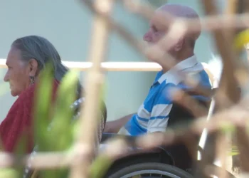 A foto mostra dois idosos em cadeira de rodas.