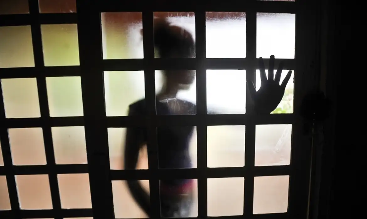 Mulher atrás de uma porta de vidro de costas, com a mão para a frente tentando impedir uma violência