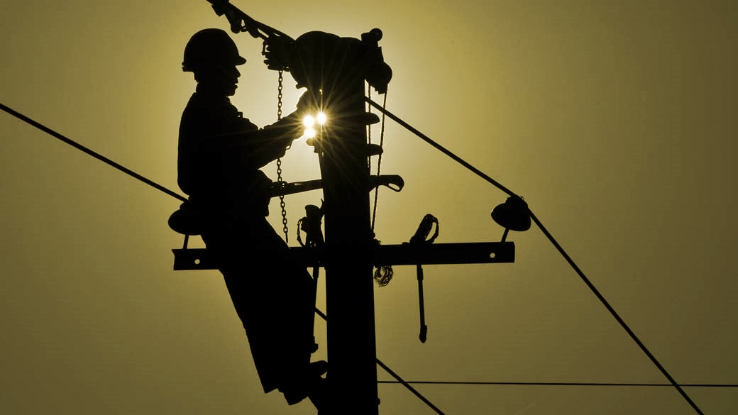 trabalhador de empresa de energia elétrica consertando fios emposte de rua