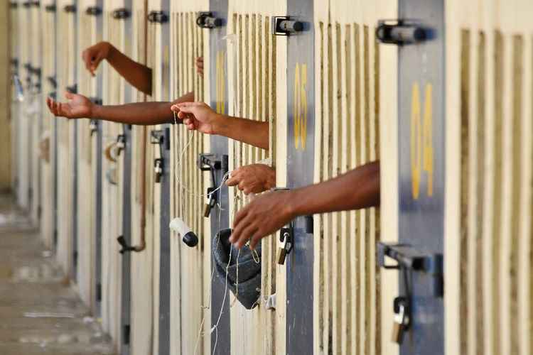 Detentos com mãos para fora dentro de celas em um complexo prisional