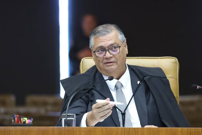 Flávio Dino sentado em sua cadeira no plenário do STF com uma caneta na mão