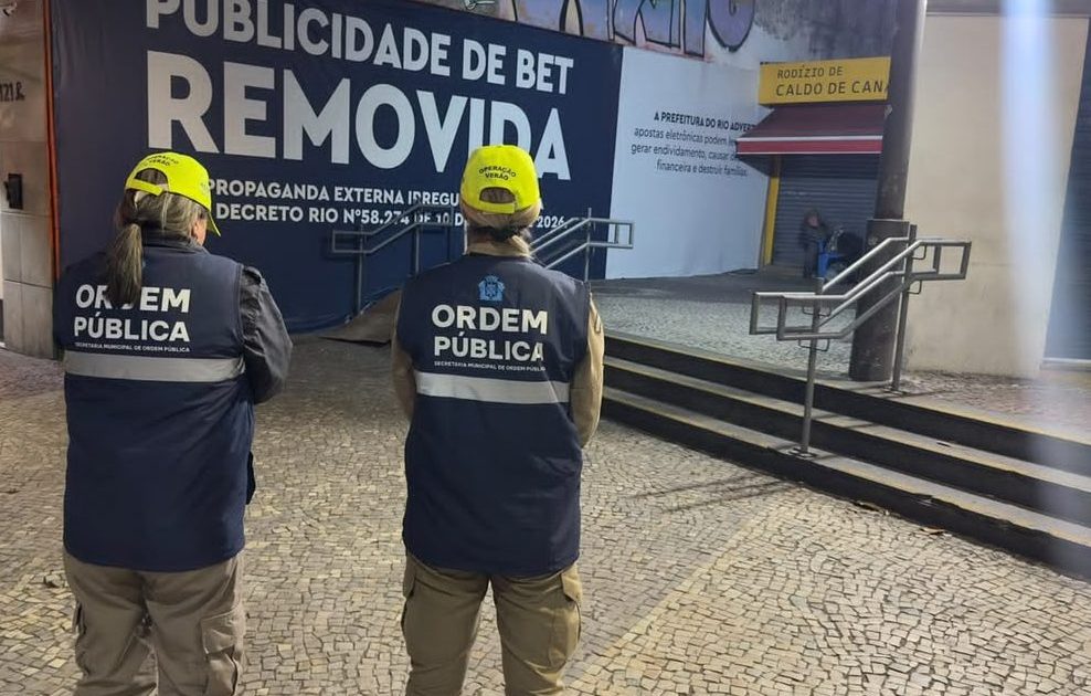 Funcionários da prefeitura diante de painel onde foi removida uma publicidade de bet
