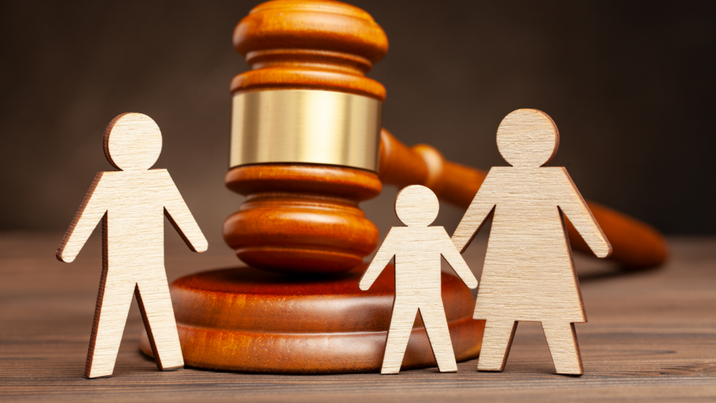 Martelo da Justiça sobre a mesa e na frente três bonecos de papel representando pai, mãe e filho ou filha