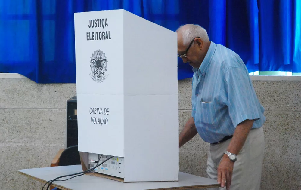 Idoso votando dentro de uma cabine de votação