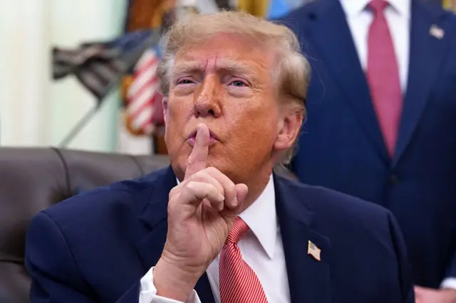 Trump com dedo sobre a boca fazendo sinal de silêncio